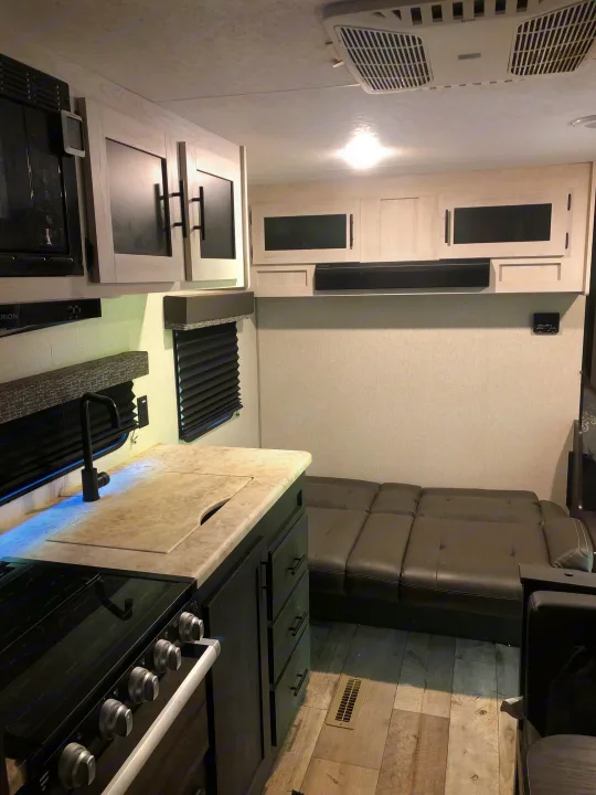 Modern RV rental interior with full kitchen (sink, stove, microwave, cabinets) and convertible sofa. Bright, well-equipped space.. KZ Sportsman SE 2022