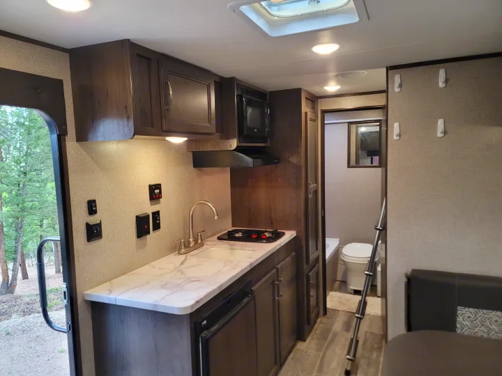 Explore a well-equipped RV rental interior, featuring a compact kitchen, full bath, and scenic outdoor views from the doorway.. Jayco Jay Flight SLX Baja Edition 2021