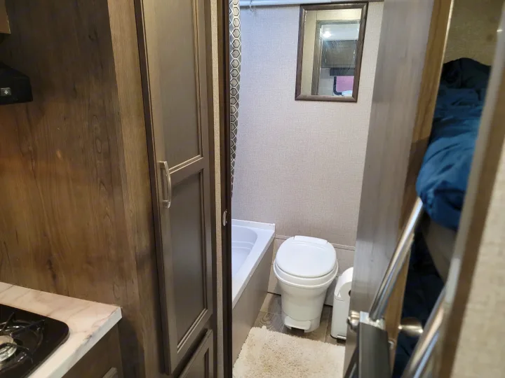Compact RV rental interior featuring a bathroom with toilet and tub, kitchen area with stovetop, and bunk beds.. Jayco Jay Flight SLX Baja Edition 2021