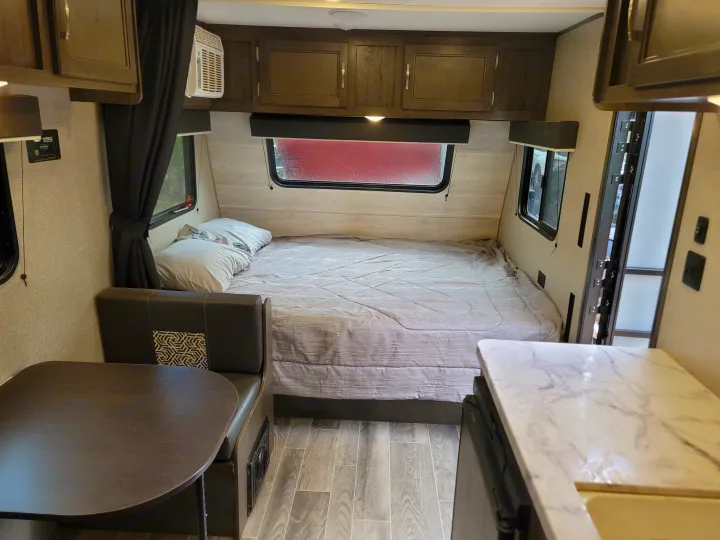 This RV rental interior shows a full bed, dining table, and partial kitchen counter, offering compact comfort.. Jayco Jay Flight SLX Baja Edition 2021
