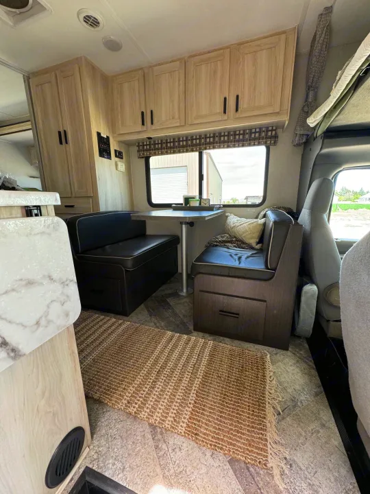 RV rental interior features a cozy dinette with black benches, light wood cabinets, and a marble-patterned kitchen counter.. Forest River Sunseeker LE 2021
