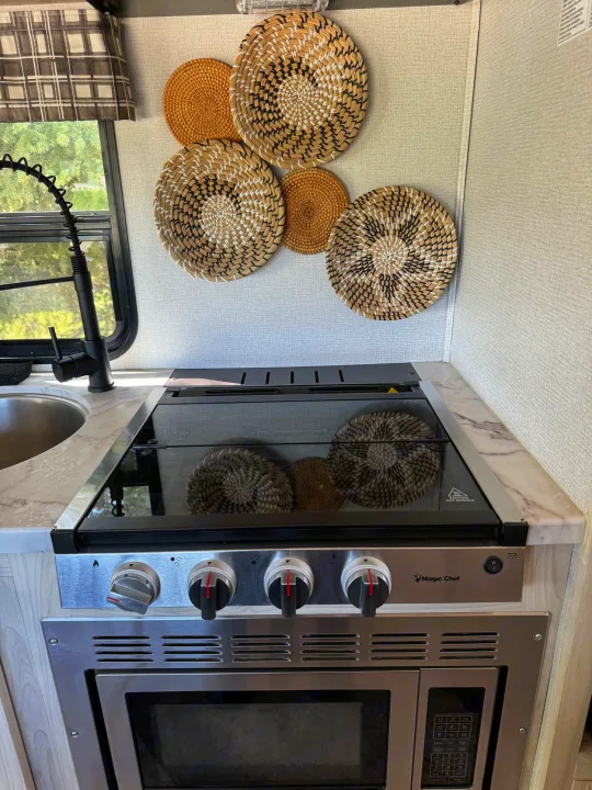 RV rental kitchen: Sink, Magic Chef stove/oven unit, modern countertops, and decorative woven wall plates on light walls.. Forest River Sunseeker LE 2021