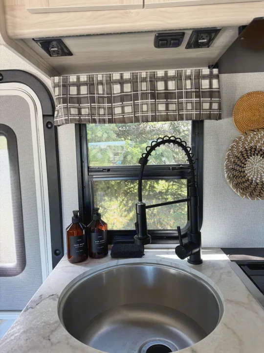 Inside an RV rental: a compact kitchen featuring a modern black faucet, stainless steel sink, and marble-look counter.. Forest River Sunseeker LE 2021