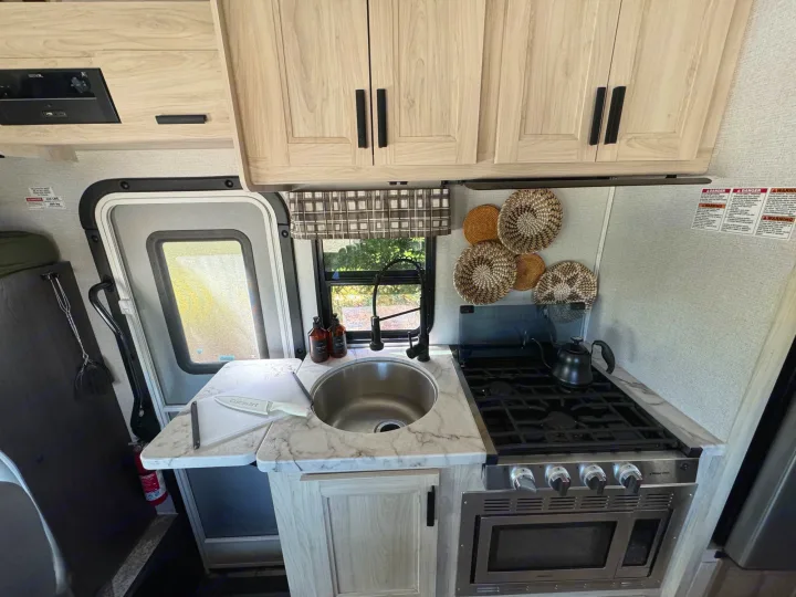 Modern RV rental kitchen with light wood cabinets, marble counters, a sink, stove, and oven. Functional & stylish.. Forest River Sunseeker LE 2021