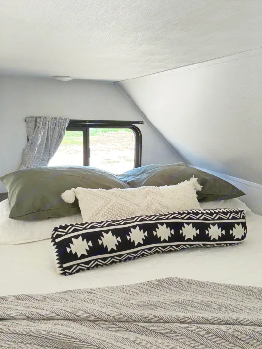 Cozy RV rental bedroom featuring a bed with textured pillows and an outdoor view.. Forest River Sunseeker LE 2021
