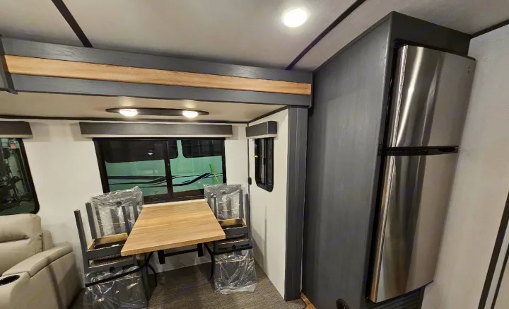 Inside a modern RV rental: a light wood dining table, wrapped chairs, and a stainless steel fridge.. Keystone RV Bullet Premier Ultra Lite 2022