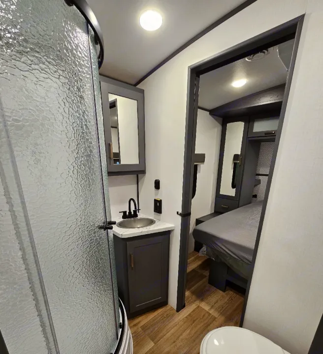 Compact RV rental bathroom with shower, vanity, and toilet, leading into the adjacent bedroom.. Keystone RV Bullet Premier Ultra Lite 2022