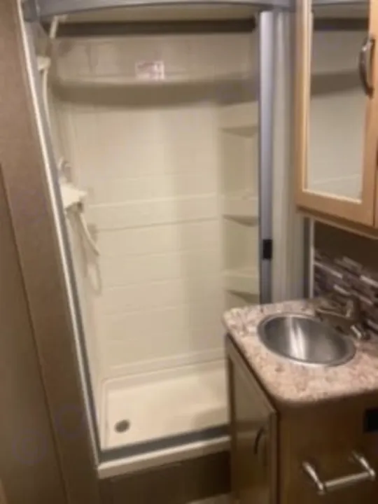 Compact RV rental bathroom featuring a clean, white shower and a vanity with a sink and mirrored cabinet.. Thor Four Winds 2020