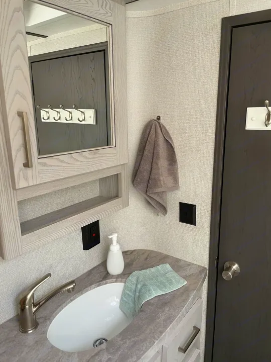 RV rental bathroom features a compact vanity with sink, modern faucet, mirror, and light gray towels on textured walls.. Keystone RV Montana High Country 2021