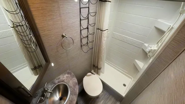 Compact RV rental bathroom: neutral tones, sink vanity, toilet, & standing shower with patterned curtain.. Thor Four Winds 2021