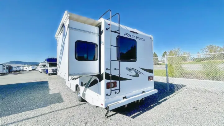White Four Winds motorhome RV rental with extended slide-out and rear ladder. Parked on a sunny gravel lot.. Thor Four Winds 2021
