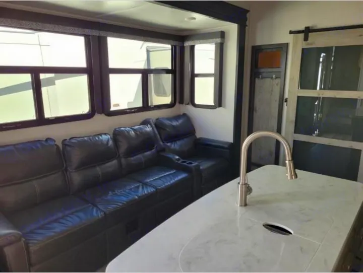 Modern RV rental living area with black leather recliners, large windows, and a sleek kitchen island.. Keystone RV Avalanche 2021