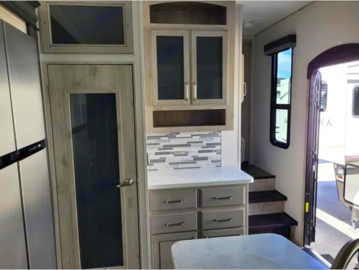 Modern RV rental interior showing a kitchen with mosaic backsplash, fridge, pantry, and steps to the upper level.. Keystone RV Avalanche 2021