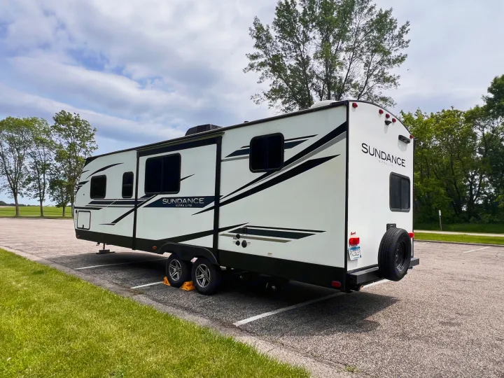 This white Sundance Ultra Lite travel trailer, an RV rental, is parked in a lot under a cloudy sky.. Heartland Sundance 2022