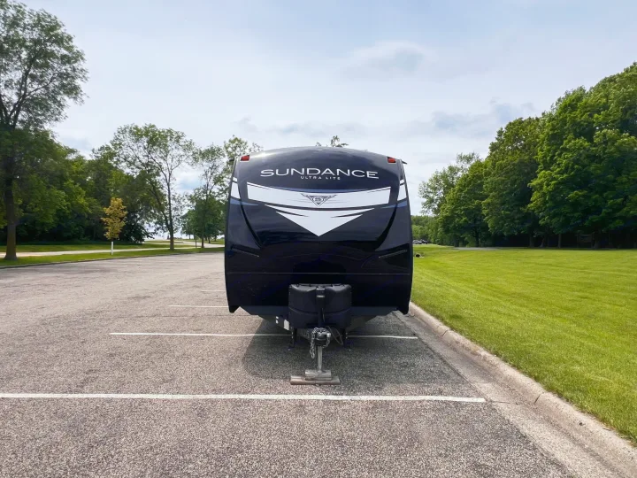 A black Sundance Ultra Lite travel trailer, a great RV rental, parked in an outdoor lot with trees and green grass.. Heartland Sundance 2022