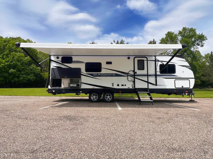 This RV rental, a white travel trailer with an extended awning and outdoor grill, is ready for your next outdoor adventure.. Heartland Sundance 2022