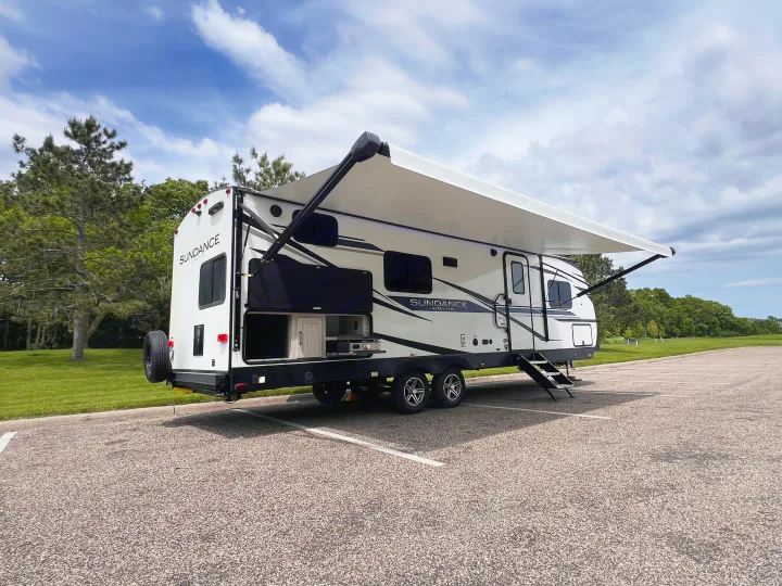 White Sundance Ultra-Lite RV rental parked with extended awning and open outdoor kitchen, ready for camping trips.. Heartland Sundance 2022