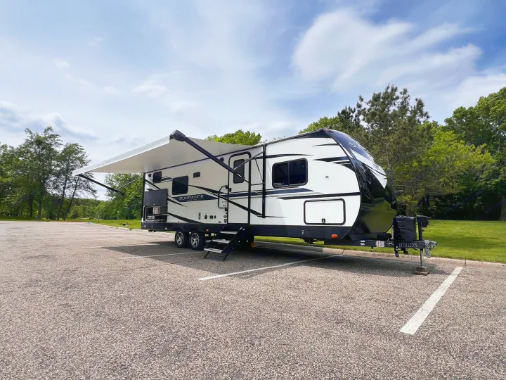 Sleek white & black Sundance Ultra-Lite RV rental, a travel trailer with awning extended, parked in a scenic lot.. Heartland Sundance 2022
