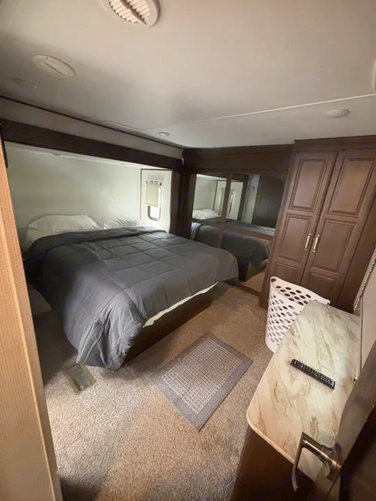 Comfortable RV rental bedroom: dark bed, white pillows, window, mirrored wardrobe, and carpeted floor.. Keystone RV Avalanche 2021
