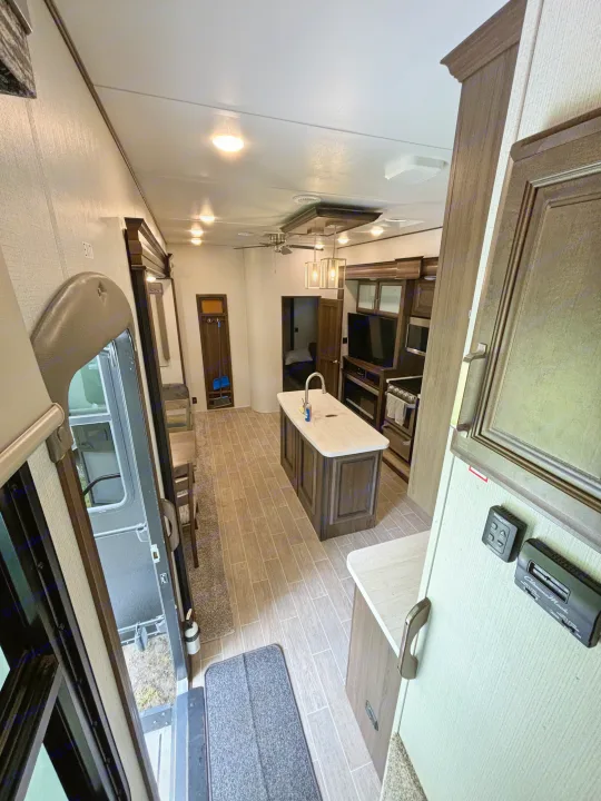 Looking into a modern rv rental's spacious interior, featuring a kitchen island, appliances, and living area.. Keystone RV Avalanche 2021