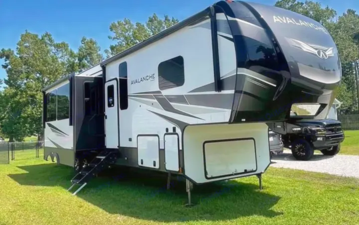 Avalanche fifth-wheel RV rental: large white & black travel trailer parked on grass with slide-outs & steps extended.. Keystone RV Avalanche 2021
