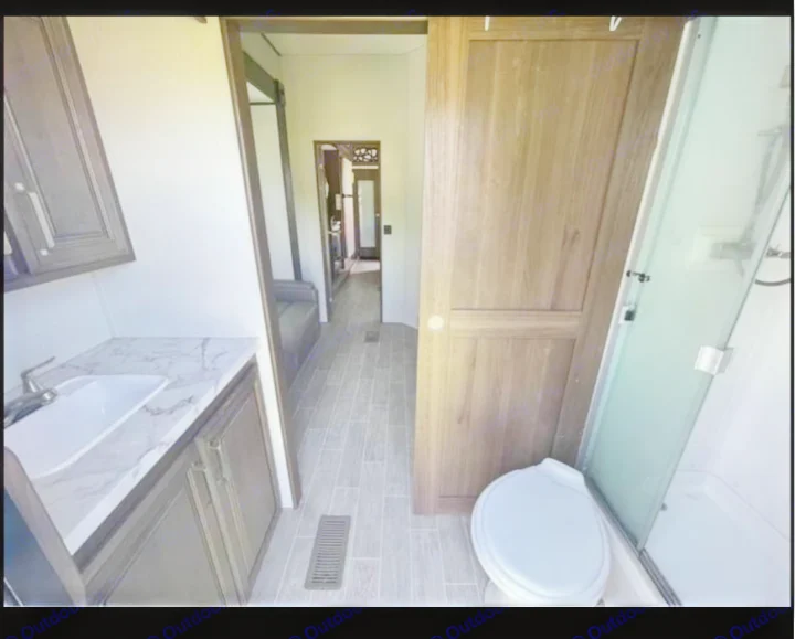 Modern RV rental bathroom: sink with marble counter, toilet, glass shower, and hallway. Clean, functional interior.. Keystone RV Avalanche 2021