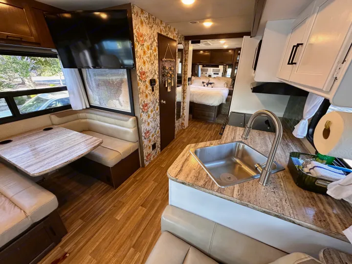 Spacious RV rental interior featuring a cozy dining area, modern kitchen with a sink, and a bedroom in the back.. Thor Motor Coach A.C.E 2018