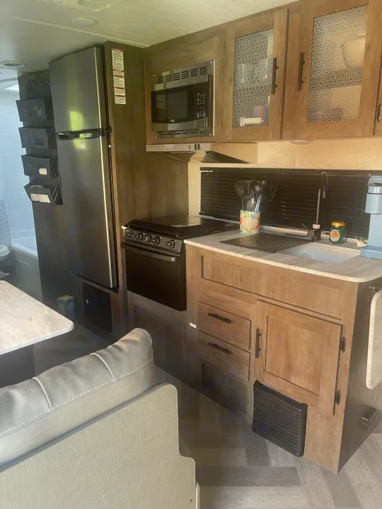 Modern RV rental kitchen featuring a full-size fridge, microwave, oven, sink, and ample cabinet storage.. Forest River Wildwood X-Lite 2021