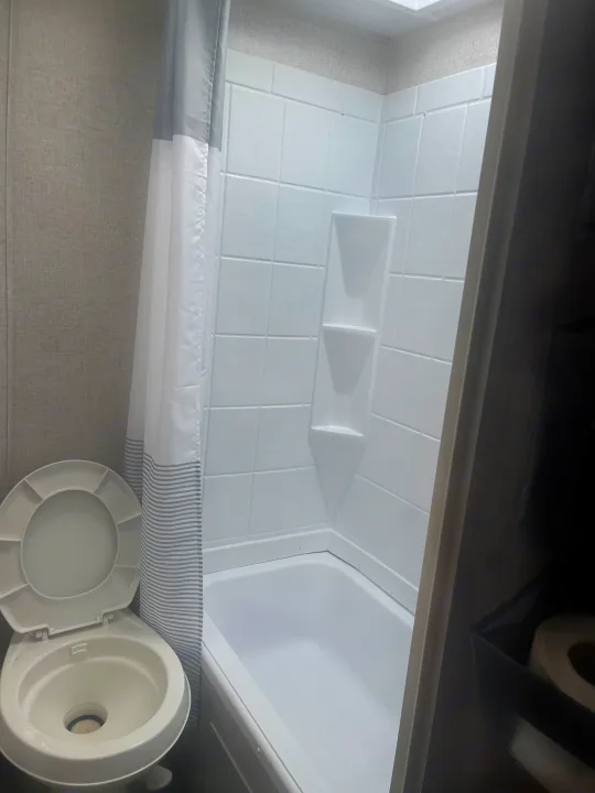 Compact RV rental bathroom with a white toilet, integrated shower/tub, and striped curtain. Ideal for travel comfort.. Forest River Wildwood X-Lite 2021