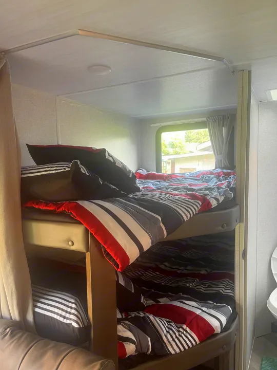RV rental interior features cozy bunk beds with striped bedding, providing a comfortable sleeping area for travelers.. Forest River Wildwood X-Lite 2021