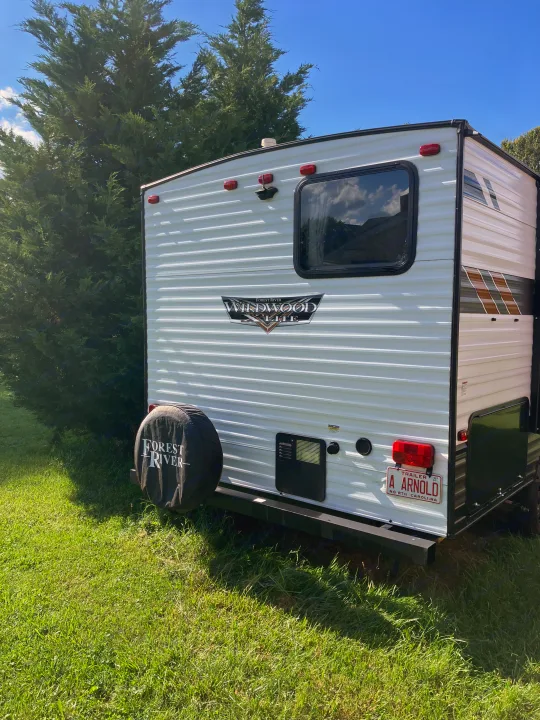 This RV rental, a Wildwood X-Lite travel trailer, sits outdoors. Its rear features a spare tire & NC plate, amidst green grass & trees.. Forest River Wildwood X-Lite 2021