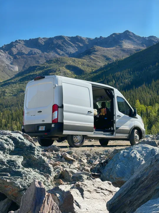 Experience van life! White RV rental parked at a rugged Alaska mountain viewpoint, open doors invite adventure.. Ford Transit 2023