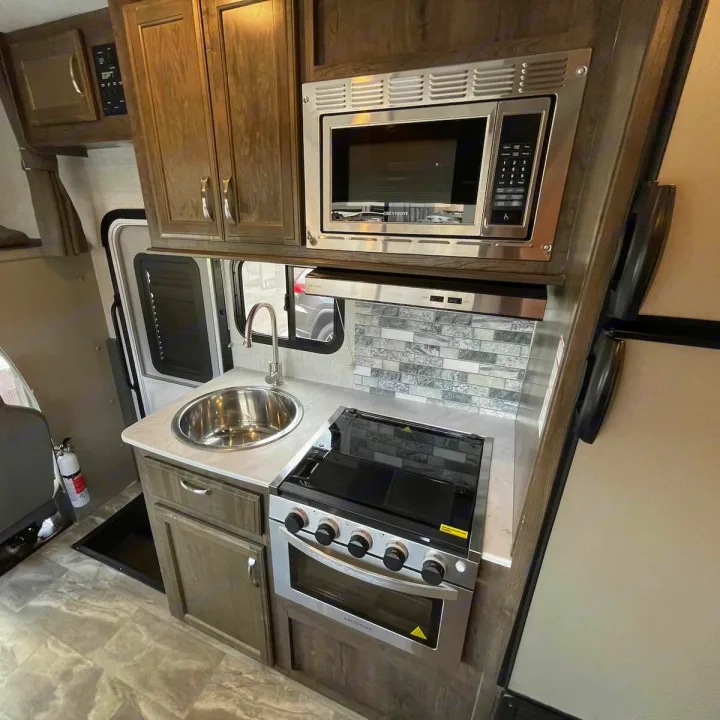 RV rental kitchen: stainless steel sink, gas stove, microwave, and wood cabinets. Ready for your next trip!. Gulf Stream Conquest 2022