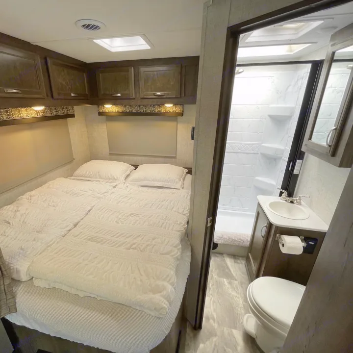 Compact RV rental interior showing a cozy bedroom and an adjacent bathroom with shower, sink, and toilet.. Gulf Stream Conquest 2022