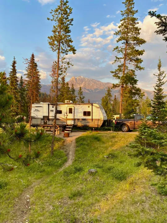 RV rental & pickup truck at a scenic forest campsite, with a dirt path leading to the trailer and mountains beyond.. Jayco Jay Flight 2022