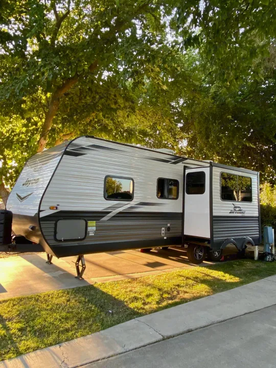 A beautiful RV rental travel trailer is fully set up on a concrete pad with green grass, surrounded by leafy trees. Ideal for camping.. Jayco Jay Flight 2022