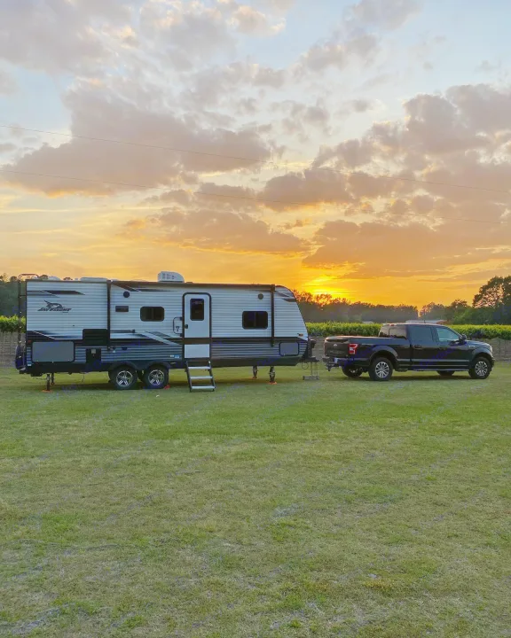 Sunset highlights an RV rental hitched to a pickup truck on a grassy field, ready for an outdoor adventure.. Jayco Jay Flight 2022