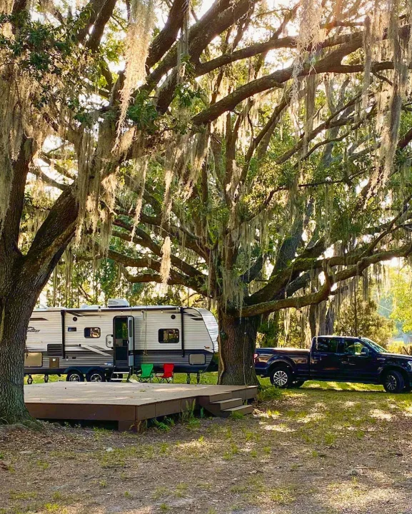 Enjoy nature with this RV rental! A travel trailer and pickup are set up at a shaded campsite under mossy oak trees with a deck.. Jayco Jay Flight 2022