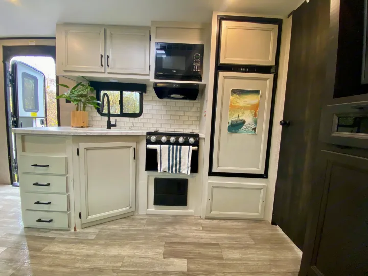 Well-equipped rv rental kitchen with light cabinetry, black fixtures, oven, microwave, and fridge for comfortable travel.. Jayco Jay Flight 2022