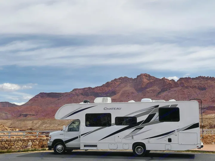 RV rental parked before stunning red desert mountains under a partly cloudy sky, perfect for a scenic road trip.. Thor Motor Coach Chateau 2024