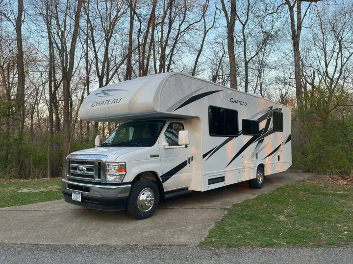 White Chateau Class C RV rental at golden hour, parked on a driveway among trees.. Thor Motor Coach Chateau 2024