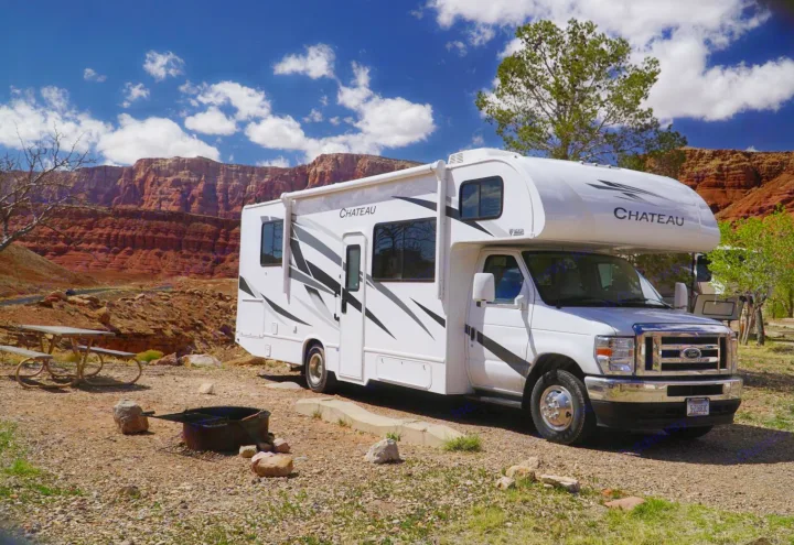 White Chateau RV rental parked at a scenic red rock campground with a picnic table & fire pit under a blue sky.. Thor Motor Coach Chateau 2024