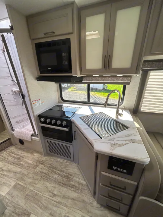 Modern RV rental interior: galley kitchen with marble counter, stove, microwave, sink, and seating area.. Thor Motor Coach Chateau 2024