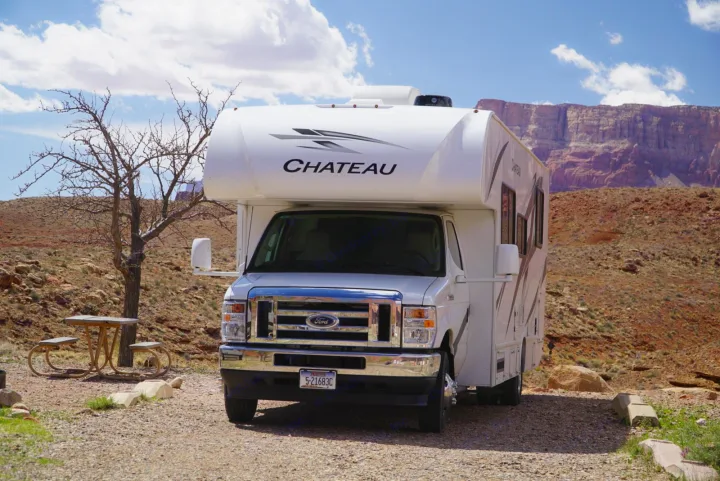 White Chateau RV rental parked in a scenic desert campground with red cliffs and a picnic table.. Thor Motor Coach Chateau 2024