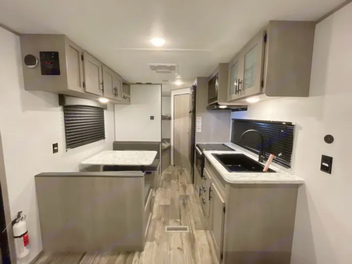 RV rental interior featuring a compact, modern kitchen with a black sink and stovetop, opposite a comfortable dining booth.. Coleman LT 274BH 2024