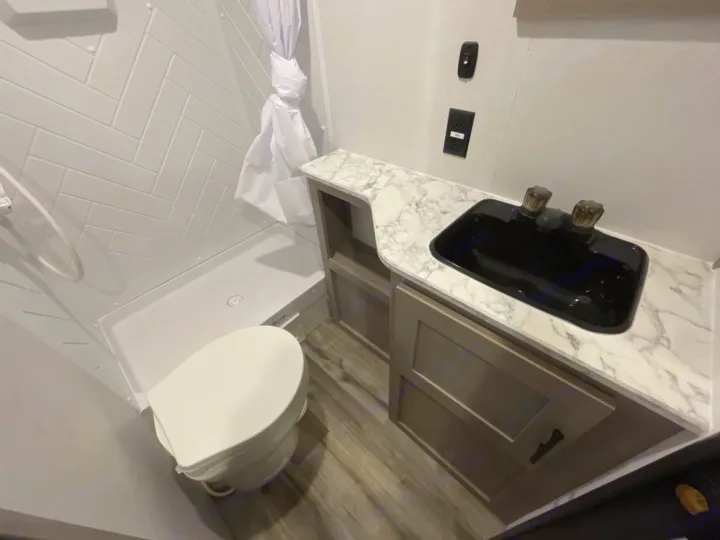 Explore your RV rental's bathroom amenities: White toilet, modern tiled shower, and vanity with a sleek black sink.. Coleman LT 274BH 2024