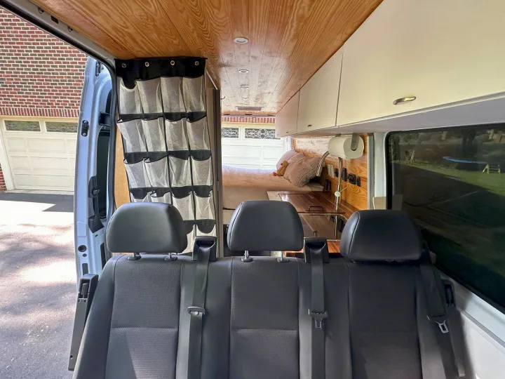 Step inside this RV rental! A custom camper van interior with rear seats, wooden ceiling, kitchen, bed, and smart storage.. Mercedes-Benz Sprinter 2021