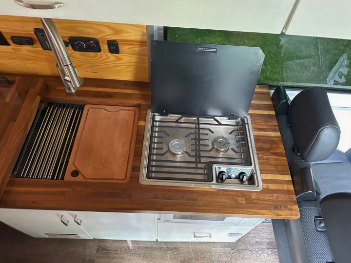 RV rental kitchen area: wooden counter, sink, and two-burner stove with controls visible. Compact and functional interior.. Mercedes-Benz Sprinter 2021