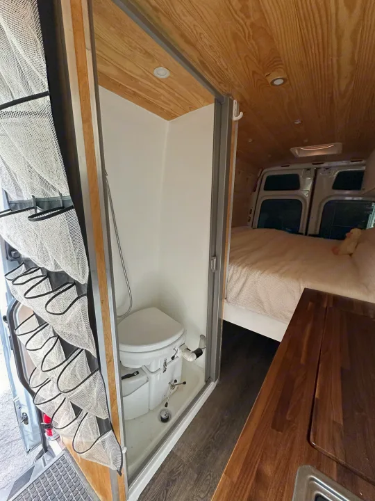 Spacious RV rental interior with a cozy bed, compact bathroom/shower, and wooden accents. Perfect camper van living.. Mercedes-Benz Sprinter 2021