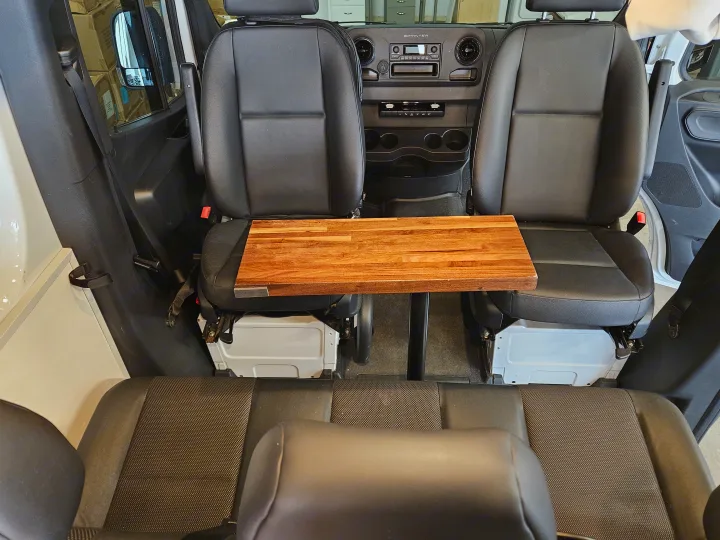 RV rental Sprinter van interior: view from rear shows front seats with a wooden table between them & a rear bench.. Mercedes-Benz Sprinter 2021